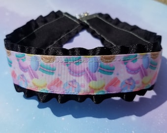 May include: Black choker necklace with a pink and white ribbon featuring a pattern of colorful macarons.