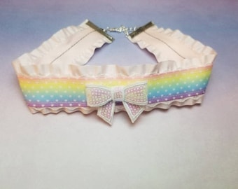May include: A pink choker necklace with a rainbow ribbon and white polka dots. The ribbon has a white bow with a sparkly texture.