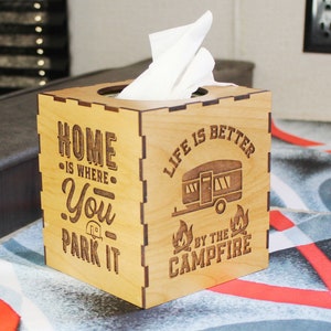 May include: Wooden tissue box cover with a camper and campfire design. The text reads "Home is where you park it. Life is better by the campfire."