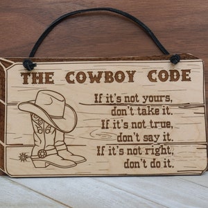 May include: A wooden sign with a cowboy hat and boots design. The sign reads "THE COWBOY CODE" and includes the text "If it's not yours, don't take it. If it's not true, don't say it. If it's not right, don't do it."