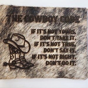 May include: A brown and white cowhide wall hanging with the text "THE COWBOY CODE" and a cowboy boot graphic. The text reads "IF IT'S NOT YOURS, DON'T TAKE IT. IF IT'S NOT TRUE, DON'T SAY IT. IF IT'S NOT RIGHT, DON'T DO IT."