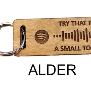 May include: Wooden keychain with a silver key ring and a clip. The keychain has a Spotify logo and a barcode with the text "Try that in a small town".