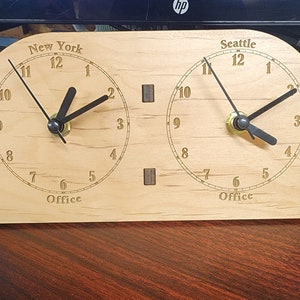 May include: A wooden clock with two faces, one for New York and one for Seattle. Each face has black hands and black numbers on a light wood background. The clock is labeled "Office" below each face.