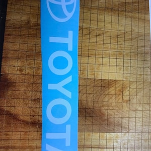 May include: A blue and white vinyl decal with the Toyota logo and the word "TOYOTA" written vertically in white.