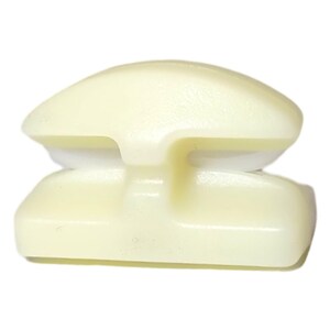 May include: A pale yellow plastic object with a rounded top and a rectangular base. The object has a curved, layered design with a central indentation. The overall shape is symmetrical and smooth.