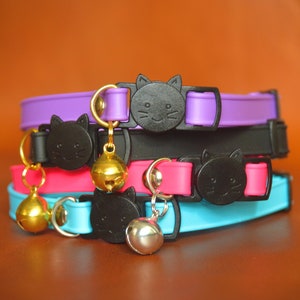 May include: A stack of four colorful cat collars with black cat head charms and gold bells. The collars are purple, black, pink, and blue.
