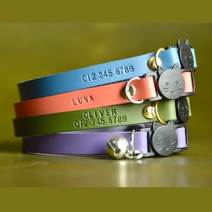 May include: Four colorful leather cat collars with engraved names and phone numbers. The collars feature a cat-shaped buckle and a bell.