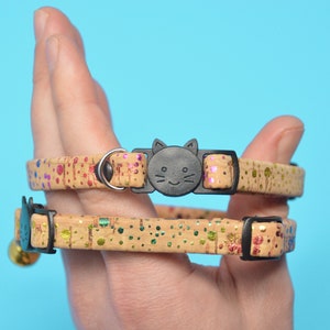 May include: Two cat collars made of cork with a colorful confetti pattern. The collars have a black plastic cat-shaped buckle and a bell.