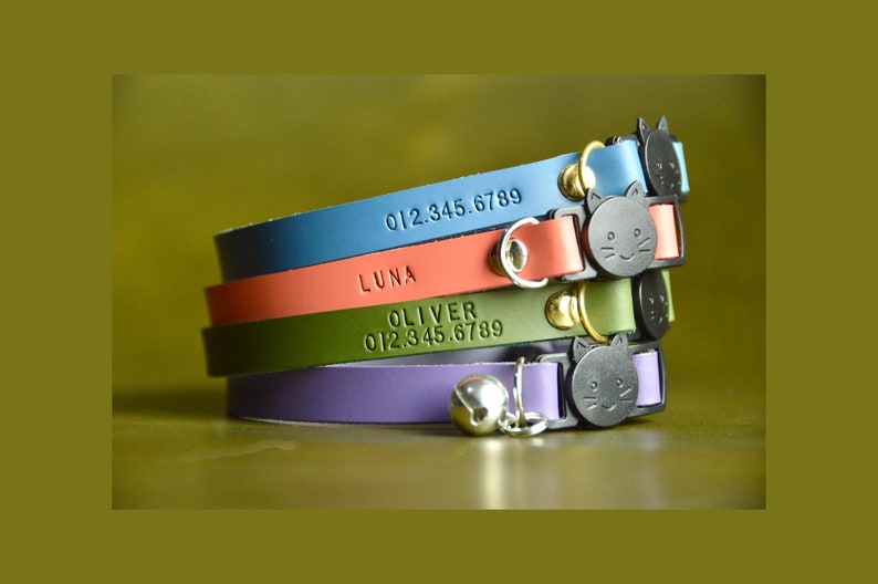 May include: Four colorful leather cat collars with engraved names and phone numbers. The collars feature a cat-shaped buckle and a bell.