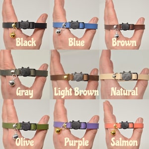 K&ouml;nnte beinhalten: Neun verschiedene farbige Katzenhalsb&auml;nder mit einem schwarzen Katzenanh&auml;nger und einer Glocke. Die Halsb&auml;nder sind in den Farben Schwarz, Blau, Braun, Grau, Hellbraun, Natur, Oliv, Lila und Lachs dargestellt.