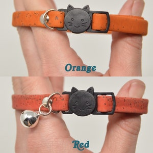 K&ouml;nnte beinhalten: Zwei Katzenhalsb&auml;nder aus Kork mit einer schwarzen Katzenkopf-Schnalle. Das obere Halsband ist orange und das untere Halsband ist rot. Das rote Halsband hat eine silberne Glocke.