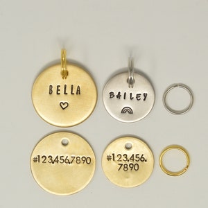 May include: Four round metal pet ID tags with different engravings. Two gold tags read "BELLA" with a heart and "#1234567890". One silver tag reads "BAILEY" with a rainbow. The other gold tag reads "#123.456.7890".