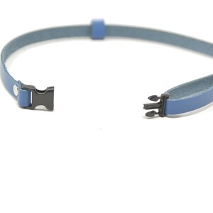 May include: A blue leather strap with black plastic clasps. The strap is open and ready to be fastened.
