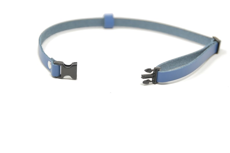May include: A blue leather strap with black plastic clasps. The strap is open and ready to be fastened.