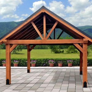 May include: A wooden gazebo with a dark roof, set against a backdrop of green grass, mountains, and a blue sky with clouds. The gazebo has a brown frame and is supported by four sturdy posts. Decorative flower pots line the front.