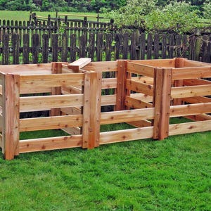 May include: Three wooden compost bins with slatted sides, arranged in a row on a grassy lawn. The bins are made of natural cedar wood and are ready for composting.
