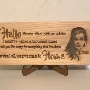 May include: Wooden sign with a laser-engraved image of Adele and lyrics from her song "Hello". The lyrics read: "Hello from the other side I must've called a thousand times to tell you I'm sorry for everything that I've done but when I call, you never seem to be Home".