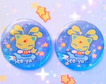 May include: Two blue and yellow round buttons with a cartoon character on each. The character is a yellow cat with blue eyes and a pink nose. The character is wearing a blue and white outfit and has a blue halo. The buttons have a blue background with white stars and the text "see ya..." on each.