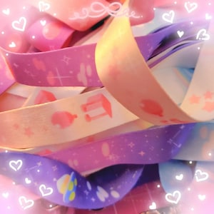 May include: A collection of colorful fabric lanyards with various pastel-colored designs, including stars, clouds, and a small house. The lanyards are made of a soft, textured fabric and are perfect for adding a touch of personality to your keys, bags, or ID badges.
