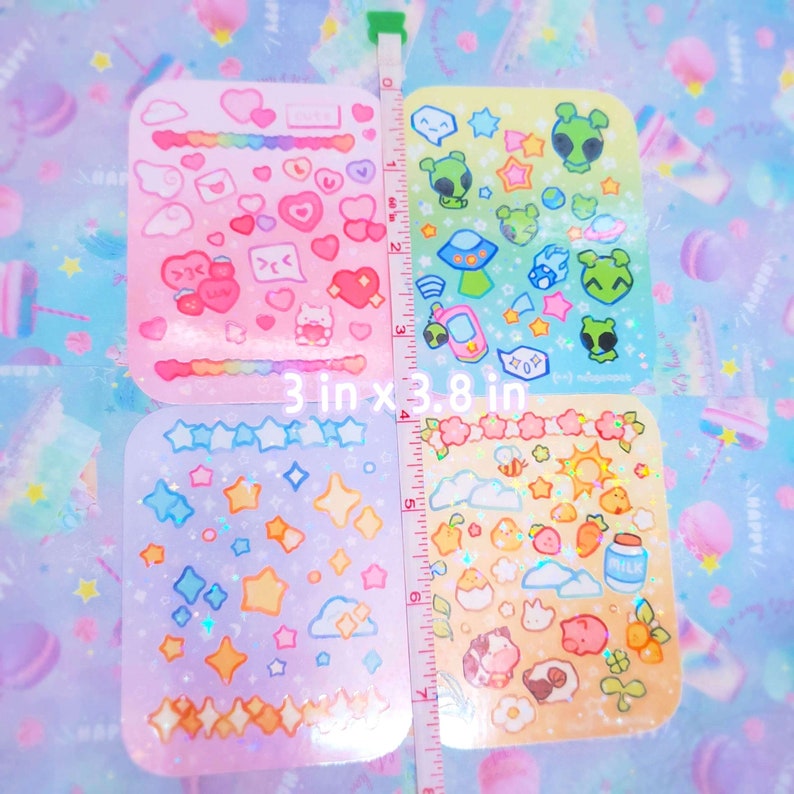 May include: Four sheets of holographic sticker paper with various cute designs. The designs include hearts, clouds, stars, aliens, bees, and other whimsical elements. Each sheet measures 3 inches by 3.8 inches.