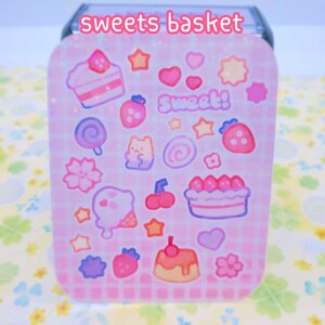 May include: A pink and white sticker sheet with a variety of sweet treats, including cake, ice cream, candy, and cherries. The sheet is decorated with stars, hearts, and swirls. The text "Sweet!" is written on the sheet.