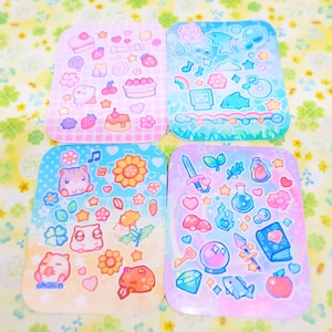 May include: Four square stickers with a variety of cute illustrations. The stickers feature a pastel color scheme with pink, blue, yellow, and purple backgrounds. The illustrations include hearts, stars, flowers, animals, and other whimsical designs.