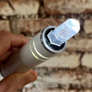 K&ouml;nnte beinhalten: Ein wei&szlig;es zylindrisches Ger&auml;t mit einem klaren Kristall oben. Der Kristall ist prismenf&ouml;rmig und hat eine silberne Metallbasis.