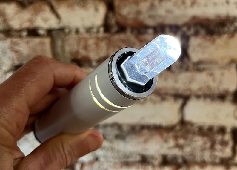 K&ouml;nnte beinhalten: Ein wei&szlig;es zylindrisches Ger&auml;t mit einem klaren Kristall oben. Der Kristall ist prismenf&ouml;rmig und hat eine silberne Metallbasis.