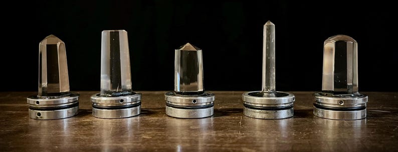 K&ouml;nnte beinhalten: F&uuml;nf klare Quarzkristallspitzen auf Metallsockeln. Die Kristalle sind in verschiedenen Formen und Gr&ouml;&szlig;en. Die Sockel sind silberfarben und haben ein dekoratives Design.