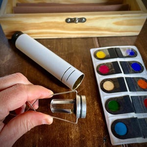 K&ouml;nnte beinhalten: Ein Satz farbige Glasfilter in einem wei&szlig;en Kunststoffgeh&auml;use. Die Filter sind rund und in verschiedenen Farben erh&auml;ltlich, darunter Rot, Blau, Gr&uuml;n und Gelb. Das Geh&auml;use hat einen schwarzen Hintergrund und ist mit der Farbe jedes Filters beschriftet.