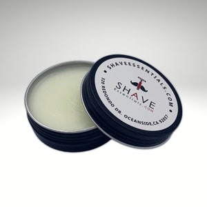 May include: A small, round, silver tin with a black lid. The lid has a white label with the text "Shave Essentials.com" and a red and black illustration of a razor and mustache. The text "320 Redondo Dr. Oceanside, CA 92057" is also on the label.