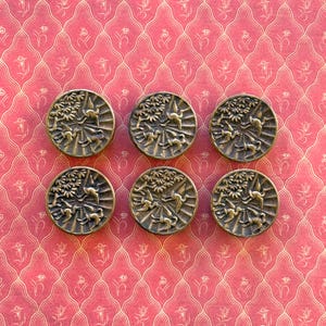 May include: Six antique brass buttons with a detailed relief design featuring birds and foliage. The buttons are round and have a slightly aged appearance, set against a patterned pink background.