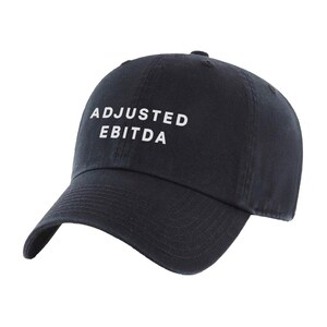 May include: A navy blue baseball cap with the words "ADJUSTED EBITDA" printed in white. The cap has a curved brim and a fabric strap closure on the back. The hat is made of a soft, durable material.