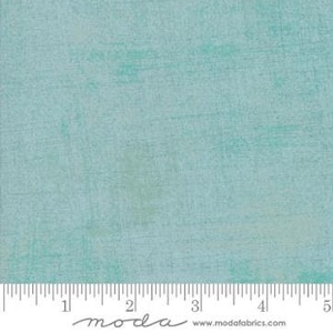 May include: A close-up of a fabric with a textured, mottled appearance. The fabric is primarily a light teal color with subtle variations in tone, creating a distressed or aged effect. The fabric is likely cotton or a similar material.
