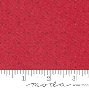 May include: Red fabric with a repeating pattern of small, dark brown dots. The fabric has a textured appearance and a ruler is visible along the bottom edge. The fabric is from Moda Fabrics.