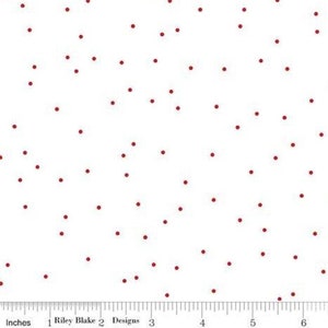 May include: White fabric with a scattered pattern of small, dark red dots. The fabric is marked with a ruler in inches.