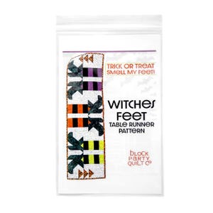 May include: A clear plastic bag containing a Halloween-themed table runner pattern. The pattern features a colorful design with black witch feet, orange, purple, and yellow stripes. Text on the bag reads "TRICK OR TREAT SMELL MY FEET!" and "WITCHES FEET TABLE RUNNER PATTERN."