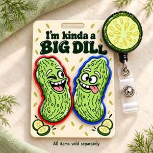 May include: A cream-colored display card featuring the text I'm kinda a BIG DILL with two cartoon pickle pins, one with a red border and one with a blue border, and a circular pickle slice badge reel with a black casing and clear clip.