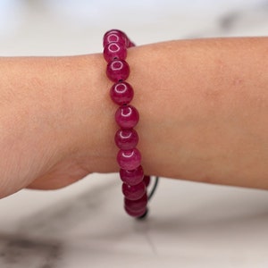 May include: A bracelet with large, round, deep red beads. The beads are strung on a black cord and worn on a wrist. The beads have a polished, glossy finish. The bracelet is a piece of jewellery.