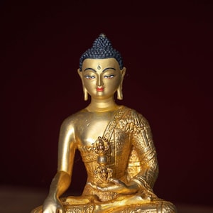 May include: A golden statue of Buddha sitting in meditation with a golden halo and a golden base. The statue is intricately detailed and has a peaceful expression.