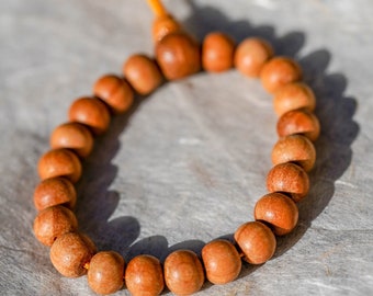 May include: A brown wooden beaded bracelet with an orange string tassel. The bracelet is made of round beads and is strung together with a thin string.