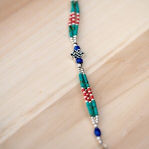 May include: A silver bracelet with turquoise, red, and blue beads. The bracelet has a silver charm in the center with a knot design.