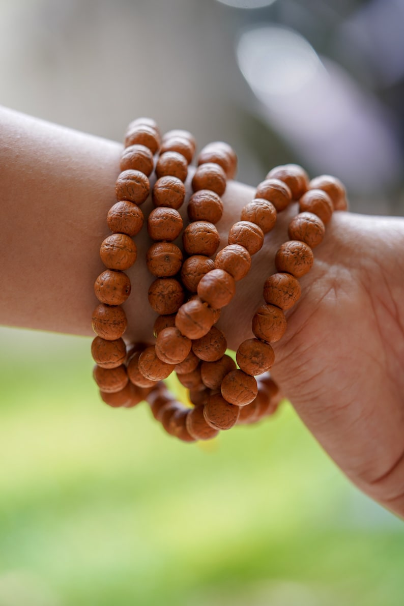 May include: A close-up of a brown wooden beaded bracelet worn on a person's wrist. The bracelet is made of multiple strands of beads, creating a layered effect.
