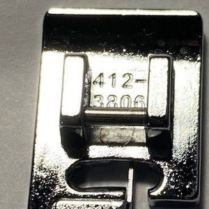K&ouml;nnte beinhalten: Ein silberner N&auml;hmaschinenfu&szlig; mit den Zahlen 412-3806 darauf gedruckt.