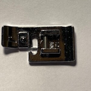 K&ouml;nnte beinhalten: Ein silberner N&auml;hmaschinenfu&szlig; mit einer Metallstange und einem kleinen Loch in der Mitte.