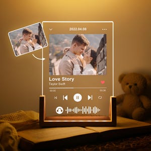 May include: A personalized LED night light featuring a photo and the text "Love Story" by Taylor Swift. The light has a wooden base and displays a couple embracing. The date "2022.04.08" is also visible.