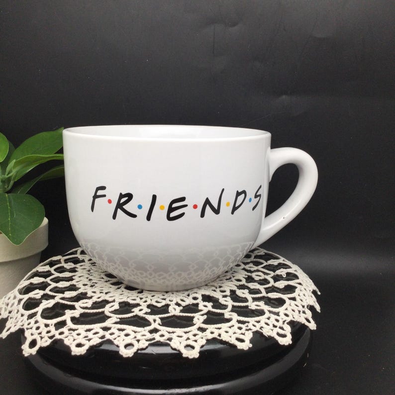 Puede incluir: Taza de cer&aacute;mica blanca de gran capacidad. La taza tiene la palabra "FRIENDS" escrita en negro con un punto despu&eacute;s de cada letra. Los puntos son de diferentes colores: rojo, amarillo, azul y amarillo.