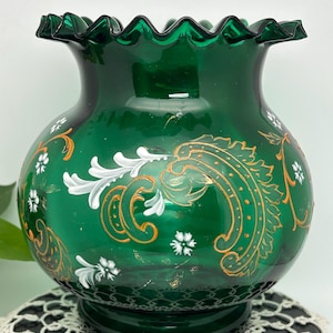 May include: A green glass vase with a ruffled rim and white and gold painted floral designs.