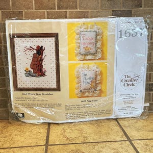 May include: A sealed plastic package containing two embroidery kits by The Creative Circle. One kit, 1651 Honey Bear Breakfast, features a bear by a tree. The other, 1657 Nap Time, includes two small pillows with the text Shh... Baby's Napping and I'm Awake Now.