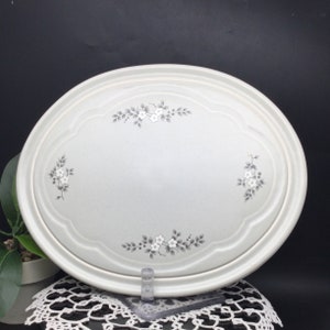 May include: A white oval serving platter with a raised rim and a floral design in gray. The design features small white flowers and gray leaves.